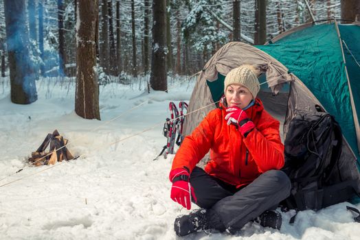 active tired woman sits near tent in winter forest