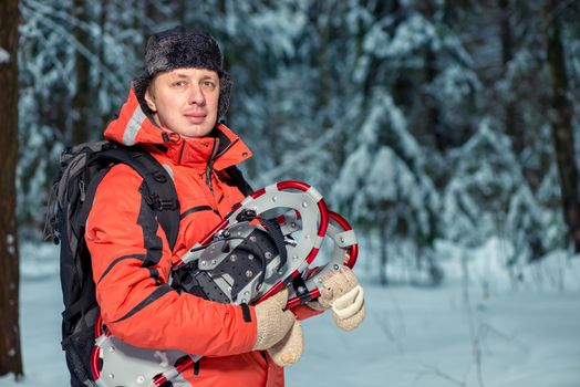 horizontal portrait of a male tourist with snowshoes in the winter forest