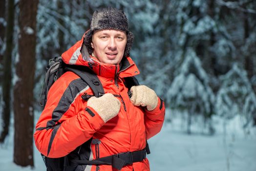 portrait of a happy tourist in a jacket hiking with a backpack in the winter forest