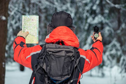 a lonely tourist is guided by the terrain with a compass and a map lost in the winter forest