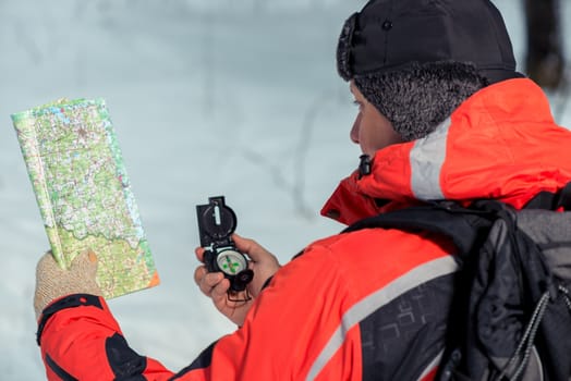 An experienced tourist with a map and a compass in the winter forest