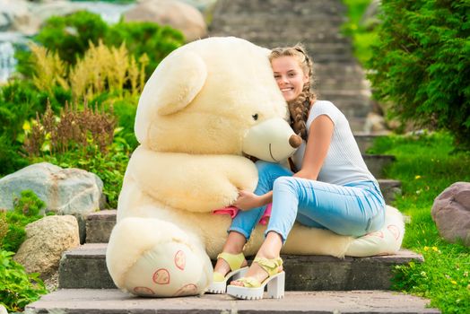 20 year old beautiful woman with a big teddy bear in the park on the stairs