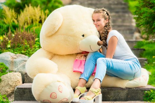 20 year old happy girl with a big teddy bear in the park on the stairs