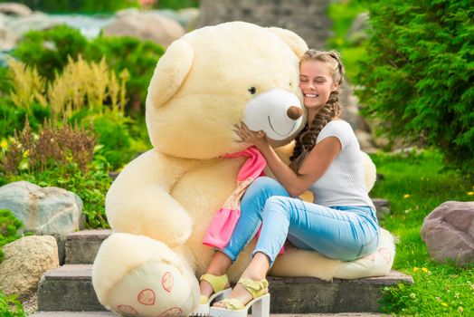 happy girl hugs her beloved big teddy bear in the park on the stairs