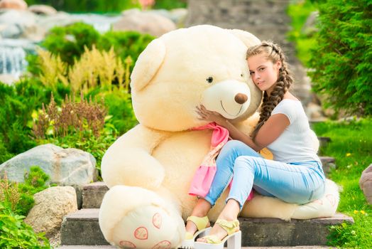 tender girl hugs her beloved big teddy bear in the park on the stairs