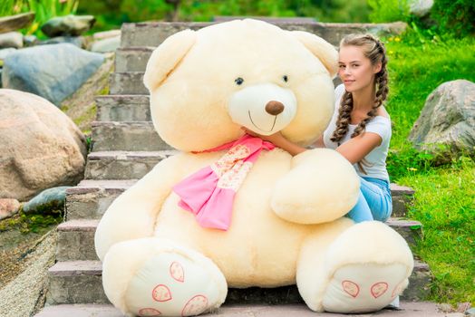 portrait of a slender girl with a huge teddy bear on the stairs in the park