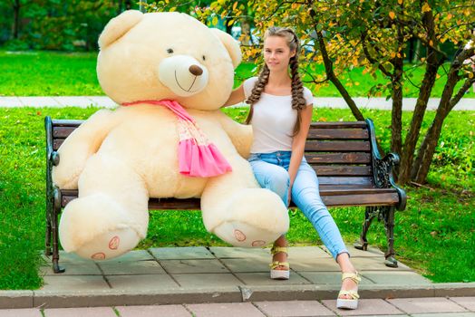 portrait of a happy girl on a bench with your favorite teddy bear in the park