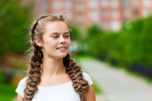 young woman in a white t-shirt with two braids in the park, horizontal close-up portrait