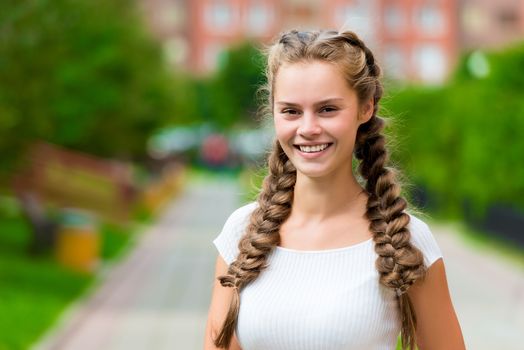 closeup happy st 20- year-old woman in a white T-shirt with two braids in the park