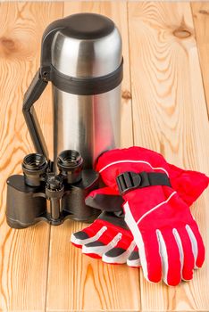 Warm gloves, binoculars and a thermos with tea ready for a difficult hike, objects on a wooden background