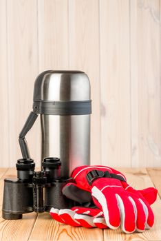 binoculars, gloves and thermos with tea ready for a difficult hike, objects on a wooden background