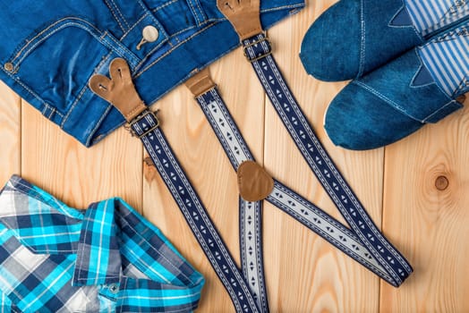 check shirt, jeans, shoes and suspenders on a wooden background top view - clothes for a boy