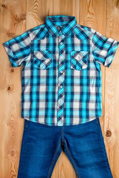 checkered blue shirt and jeans for boy set on a wooden floor top view
