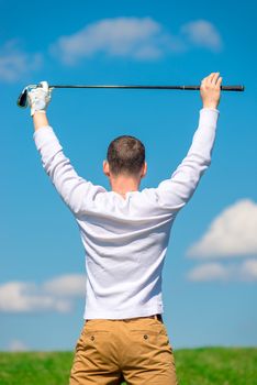 professional golfer rejoices in victory with a raised golf club over his head in the field