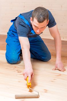 skilled young worker paint roller on a wooden floor in the house