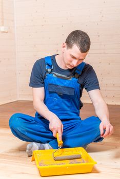 a man in overalls paint the floor in a wooden house