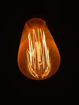 Close up one modern design electric light bulb over dark black background, low angle view