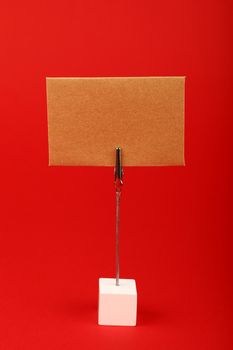 Blank brown kraft cardboard paper parchment sign with copy space on metal and wooden note holder over red background, front side view
