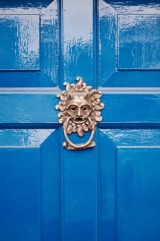 Metal gold knocker on blue door. Sunny face.