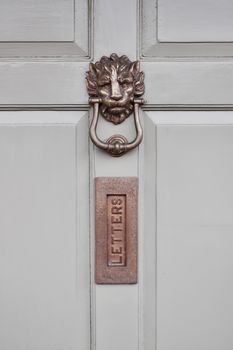 Metal gold lion knocker on white doors near letters metal whole.