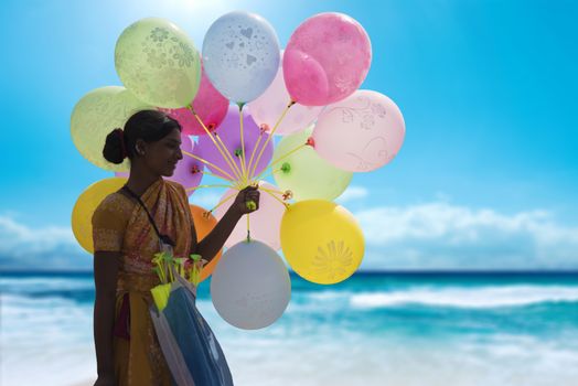 Indian hawker holding a bunch of colorful balloons at a beach and selling them to make a living.