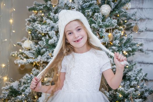 Cute girl in white hat under Christmas tree