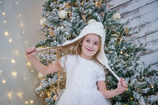 Cute girl in white hat under Christmas tree