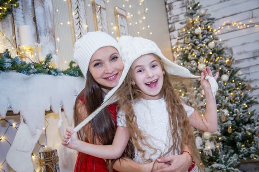 Cute girl in white hat with mother under Christmas tree