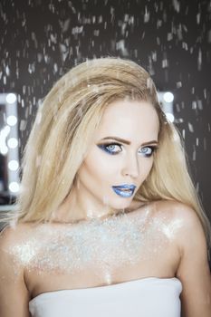 Winter Beauty Woman. Christmas Girl Makeup. Holiday Make-up. Snow Queen High Fashion Portrait over Blue Snow Background. Eyeshadows, False Eyelashes and Crystals on the Lips. Copy Space for Your Text.