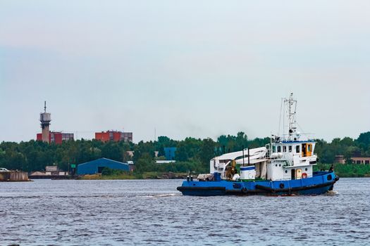 Blue tug ship moving to the cargo terminal. Industrial services