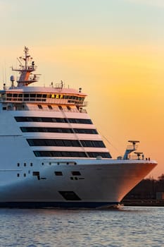 White passenger ship moving against the orange sunset sky