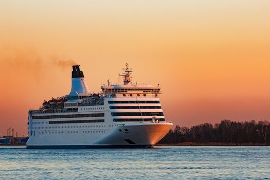 White passenger ship moving against the orange sunset sky