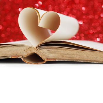 Pages of open book rolled in heart shape on glitter background