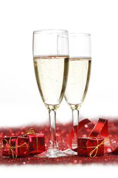 Glasses with Champagne and gifts on red glitters isolated on white background