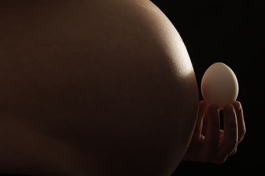 Close-up of an abdomen of a pregnant woman with chicken egg in front of it.