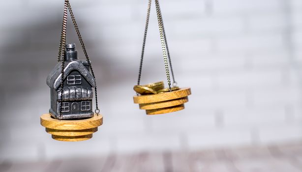 Stack of coins and a small house on the scales. The concept of choice, cash savings and purchase of real estate