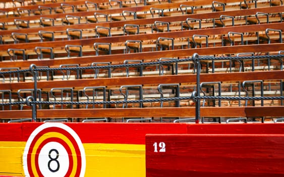 detail of the seats inside an ancient Spanish arena with wooden seats and barriers with the colors of the Spanish flag