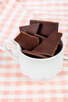 slices of chocolate bar in white cup on tablecloth.
