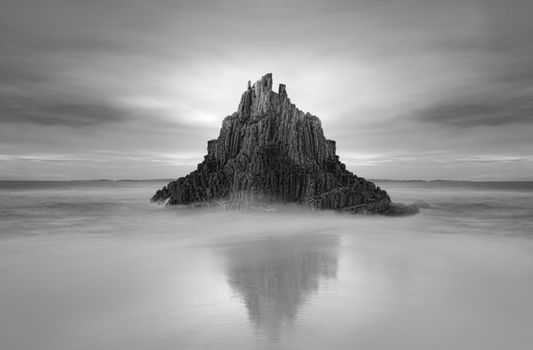 Moody sky over Pyramid Rock sea stack with tidal reflection