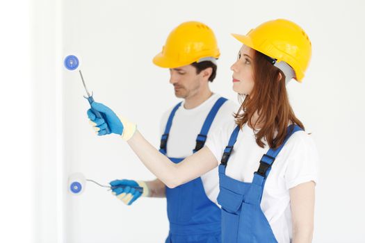 Two young workers in uniform painting the wall