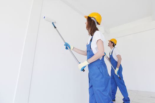 Two young workers in uniform painting the wall