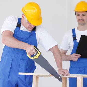 Worker works with handsaw, foreman on background