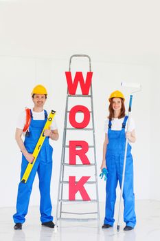Happy couple in uniform holding tools and ladder with work letters