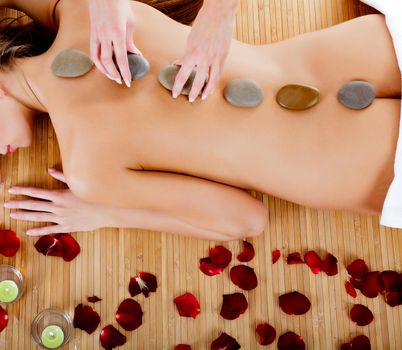 Woman at spa center, naked female back with hot stones on it