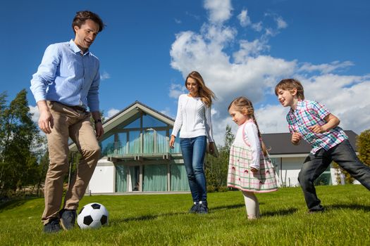 Family with children playing soccer on lawn near their house