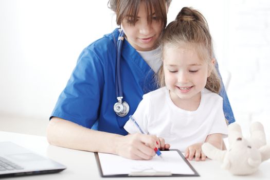 Child patient and young female doctor writing diagnosis