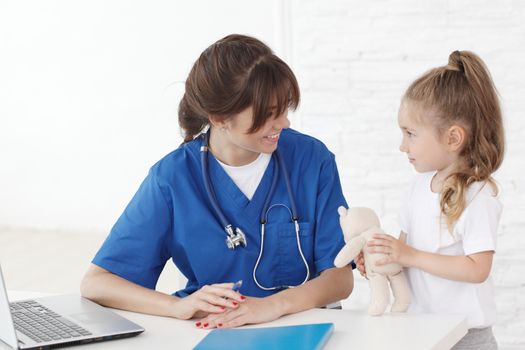 Young smiling female doctor and her little patient with teddy bear