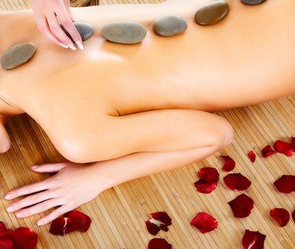 Woman at spa center, naked female back with hot stones on it