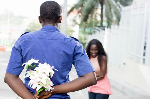 young man hides a flower in his back and give it to the young woman in surprise.