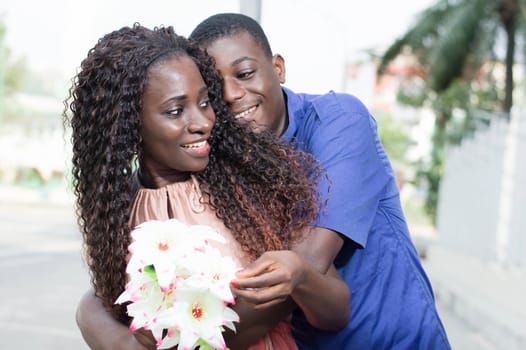 This happy young man offering a flower to his girlfriend that he embraces.